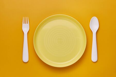 Plastic white cutlery set with yellow background. Top viewの写真素材