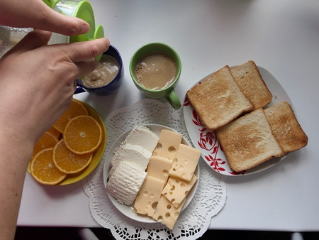 A woman pours coffee into cups. Next to breakfast products: hard and soft cheese, toast with butter...