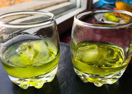 Two glasses of absinthe with burnt sugar and ice stand on a stand near the window of the apartment.の素材