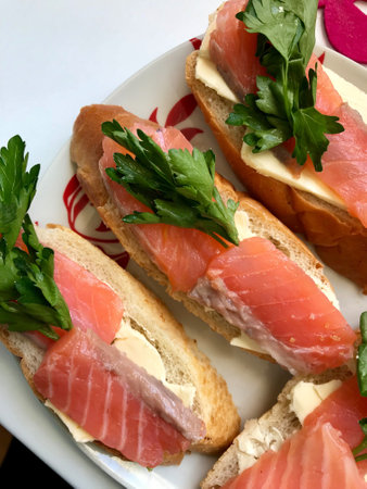 Sandwiches with salmon and greens. Pieces of fish are laid on a bread baguette, oiled. Decorated with fresh parsley.の素材