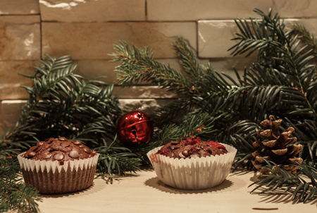 Two chocolate cupcakes in paper, a red christmas bell, a pine cone and some green pine branchesの写真素材