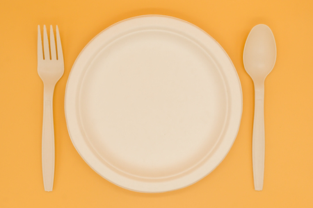 paper plate with fork and spoon on orange background in top viewの写真素材