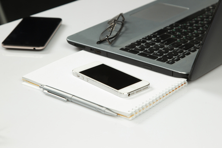 laptop, phone, notepad, pen, glasses on a white tableの写真素材