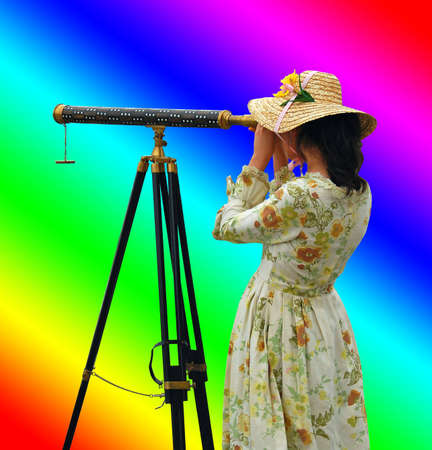 Girl in fancy dress and hat looking through telescope with background of rainbow colors.の写真素材