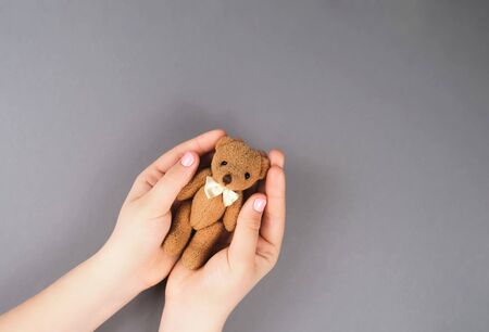 Hands of a girl with a manicure with a teddy bear on a gray background top viewの写真素材