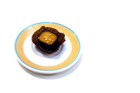 Chocolate candy with orange filling on white isolated background. On a beige-blue plate. Side view,...