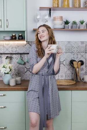 Beautiful girl in pajamas in the kitchen with a big cup, pastel colorsの写真素材
