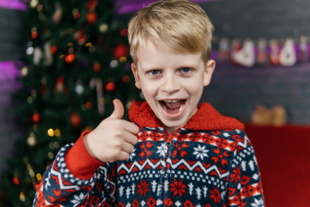 handsome and cute boy in christmas pajamas showing thumbs up, christmas background with christmas treeの写真素材