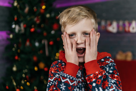 handsome and cute boy in christmas pajamas is surprised, christmas background with christmas treeの写真素材
