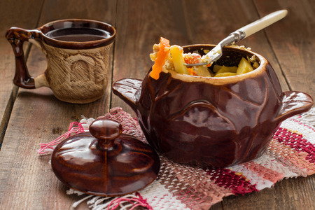Pot of stewed chicken and vegetables, ceramic mug on the wooden background. Selective focus