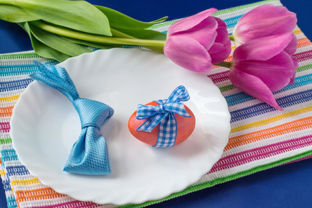 Easter table setting: a plate of eggs and rabbits out of napkins, tulips against a bright background