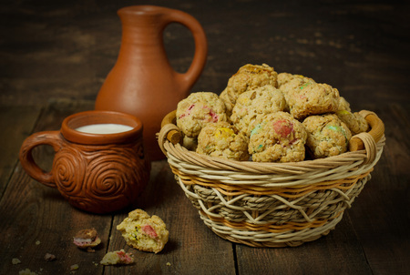 Oatmeal cookies with dragee in a basket, crock and a mug with milk on a wooden background.  Selective focusの写真素材