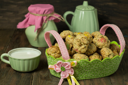 Oatmeal cookies with dragee in a basket, jug, kettle and cup with milk on a wooden background. Selective focusの写真素材