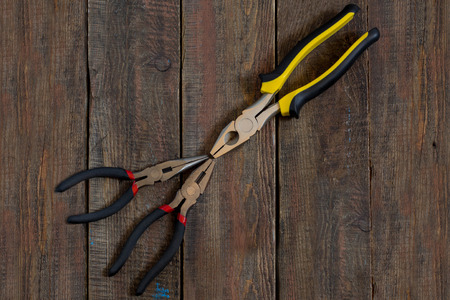 Pliers with rubber handles, decorated with yellow and red accents on a wooden surface