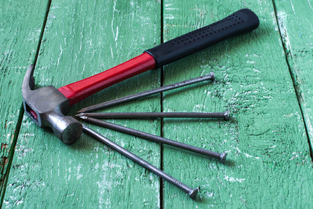 Nails and hammer with black and red handle on green wooden surface