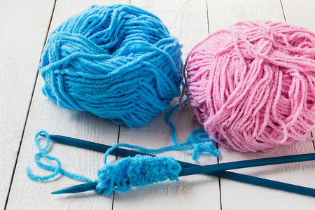 Blue and pink skeins of yarn, knitting needles on a white wooden background