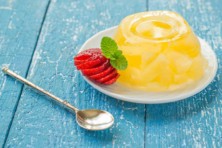 Delicious cold jelly with pineapple, sliced strawberry, mint, dessert spoon on a blue wooden table....