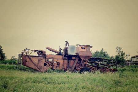 Old rusty harvester thrown on the field in the grass. Tinted photosの写真素材