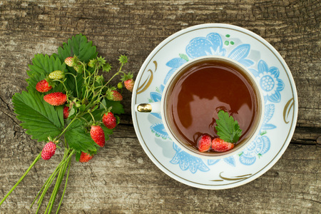 Bouquet with strawberries and strawberry tea in a cup with a national ornament on the wooden background crackedの写真素材