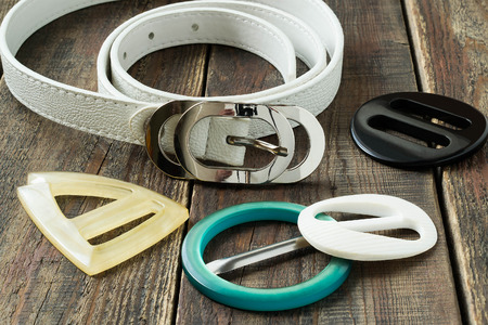 White leather womens belt and colorful buckles on the wooden table. Selective focus