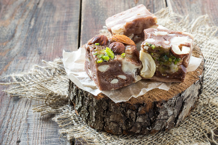 Three slice of delicious chocolate fudge with lots of different nuts on a rough wooden stand....