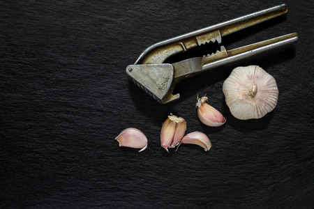 Garlic (head and clove) and the old press on slate surfaceの写真素材