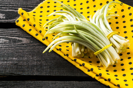 Prevention spring beriberi: bunches young shoots of ramson on yellow fabric and a dark wooden table....