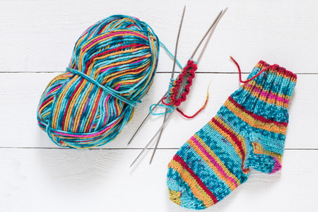 Skein of multi-colored yarn, beautiful knitted socks, knitting with spokes on white wooden tableの写真素材