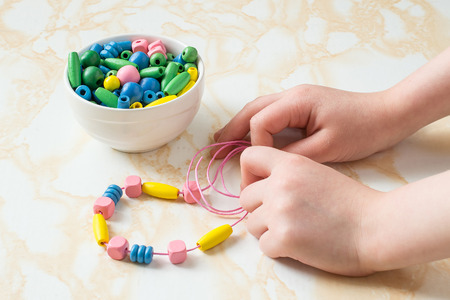 Children's hands to collect different colored wooden beads on a stringの写真素材
