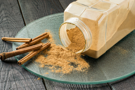 Ground cinnamon powder in jar and cinnamon sticks on glass plate on wooden tableの写真素材