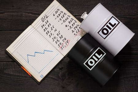 Concept of price decline for oil. Two barrels of oil and notebook with the prices and scheduleの写真素材