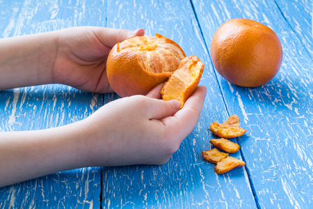 Children's hands peeling tangerine on a blue wooden tableの写真素材