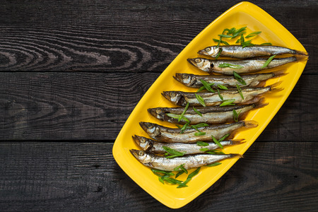 Smoked capelin with green onions on yellow plate on dark wooden background. Top viewの写真素材
