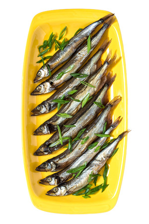 Smoked capelin with green onions on yellow plate isolated on white background. Top viewの写真素材