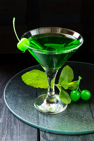 Green cocktail with maraschino cherry in a martini glass on a glass tray and dark backgroundの写真素材