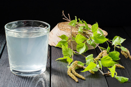 Cold fresh birch juice in a glass and birch branches on a dark backgroundの写真素材