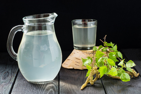 Cold fresh birch juice in a jug and glass, birch branches on a dark backgroundの写真素材