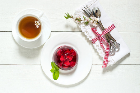 Delicious cherry jelly with whole berries on a plate, tea and blooming cherry branch on a white...