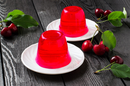 Delicious cherry jelly and ripe cherries with leaves on a dark wooden table. Selective focusの写真素材