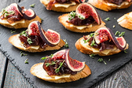 Canape or crostini with toasted baguette, cheese, onion jam, figs and fresh thyme on a slate board. Delicious appetizer, ideal as an aperitif. Selective focusの写真素材