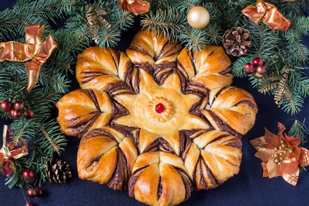 Creative homemade cake of yeast filled with chocolate. The original festive cake in the form of star on the background of branch Christmas tree with decoration on a blue backgroundの写真素材
