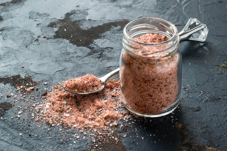 Special pink Adygei salt with spices (Russia) in a glass jar and spoon on a dark textured...