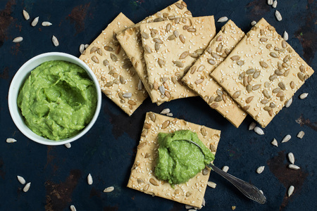Homemade wholegrain crackers with sesame, sunflower seeds and guacamole on the old blue textured...