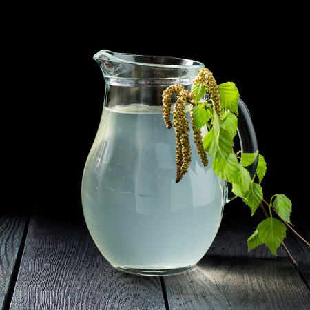 Spring useful vitamin drink. Fresh cold birch juice in a glass and birch branches on a dark background. Concept of healthy and vitamin food. Square imageの写真素材