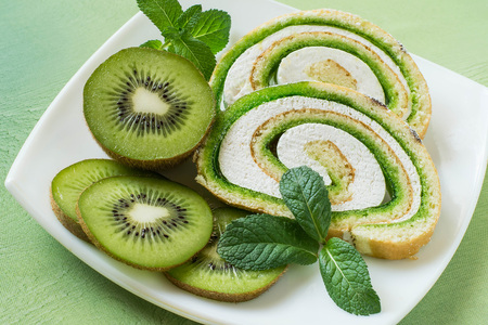 Delicious cake roll with kiwi marmalade and marshmallow. Sliced rolls on a plate, fresh kiwi and mint. Tasty fruit dessertの写真素材