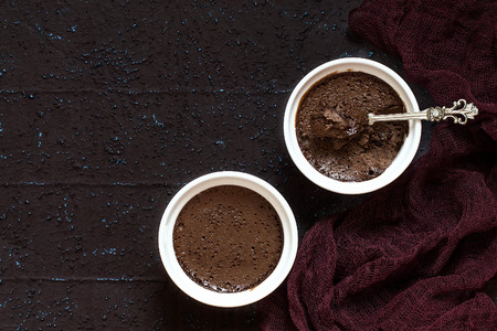 Delicate air chocolate dessert with cream and dried prunes in cups on brown textured background with gauze napkin. Copy spaceの写真素材