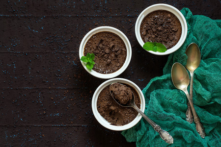 Delicate air chocolate dessert with cream and dried prunes in cups, spoons on brown textured background with gauze napkin. Dessert is sprinkled with chocolate shavings, decorated with mint. Copy spaceの写真素材