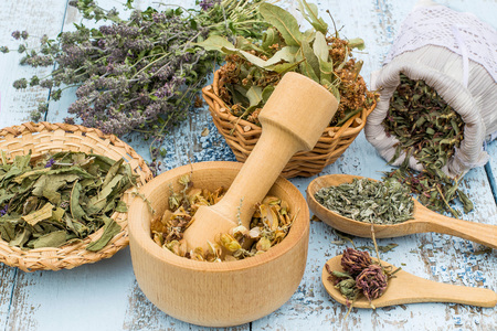 Various dried meadow herbs on light old wooden table. Dried medicinal plants in bag, basket, mortar and in bundle. Preparing medicinal plants for phytotherapy and health promotionの写真素材
