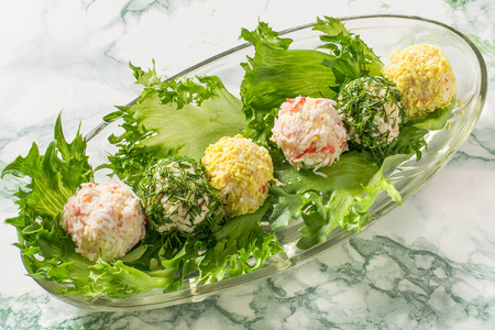 Small snack balls on lettuce. Tasty balls of cream cheese with aromatic herbs, surimi, garlic and egg on glass oval plate. Delicious appetizer for party or banquet. Festive foodの写真素材