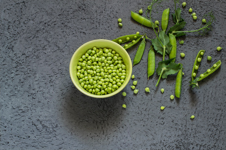 Branch of fresh green peas with pods and leaves near bowl with peas on gray textured background. New harvest of organic green peas. Vegetarian and healthy food. Top viewの写真素材